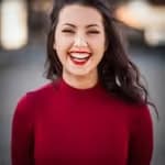 Lächelnde Frau mit roten Lippen und dunklen Haaren, die einen roten Pullover trägt.