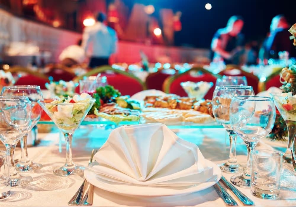 Eleganter gedeckter Tisch mit gefaltetem weißen Servietten, Gläsern und Salatgläsern bei einer festlichen Veranstaltung.