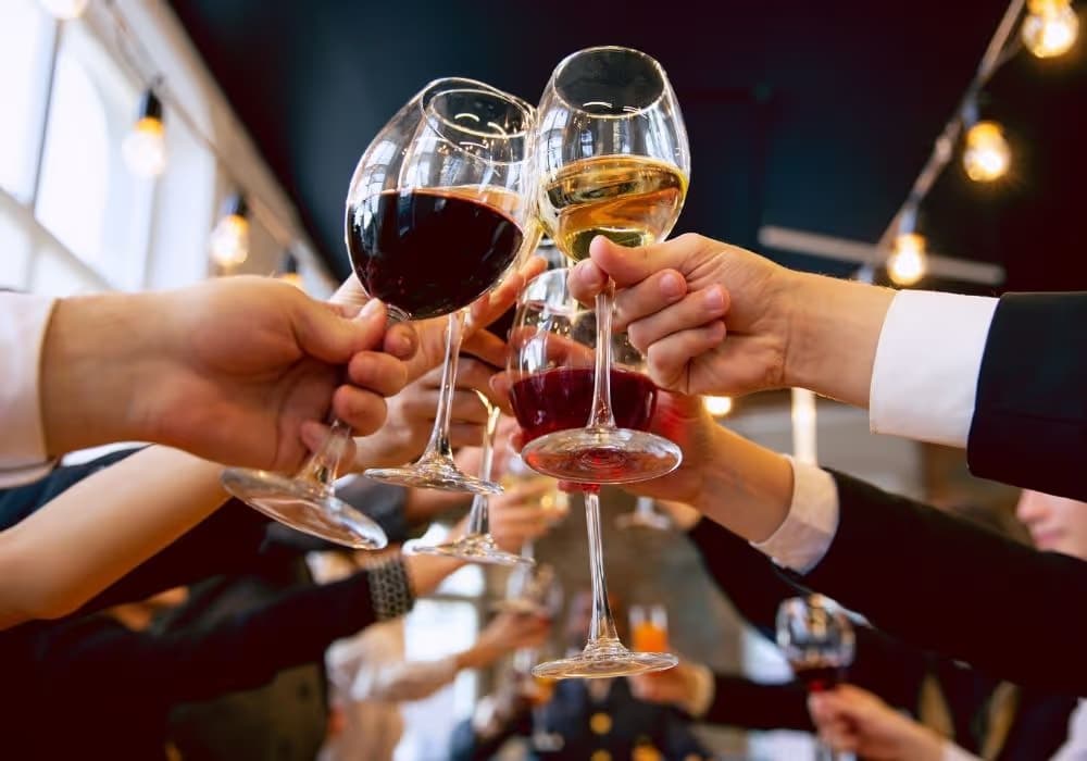 Menschen stoßen mit Weingläsern gefüllt mit rotem und weißem Wein in einem festlichen Ambiente an.